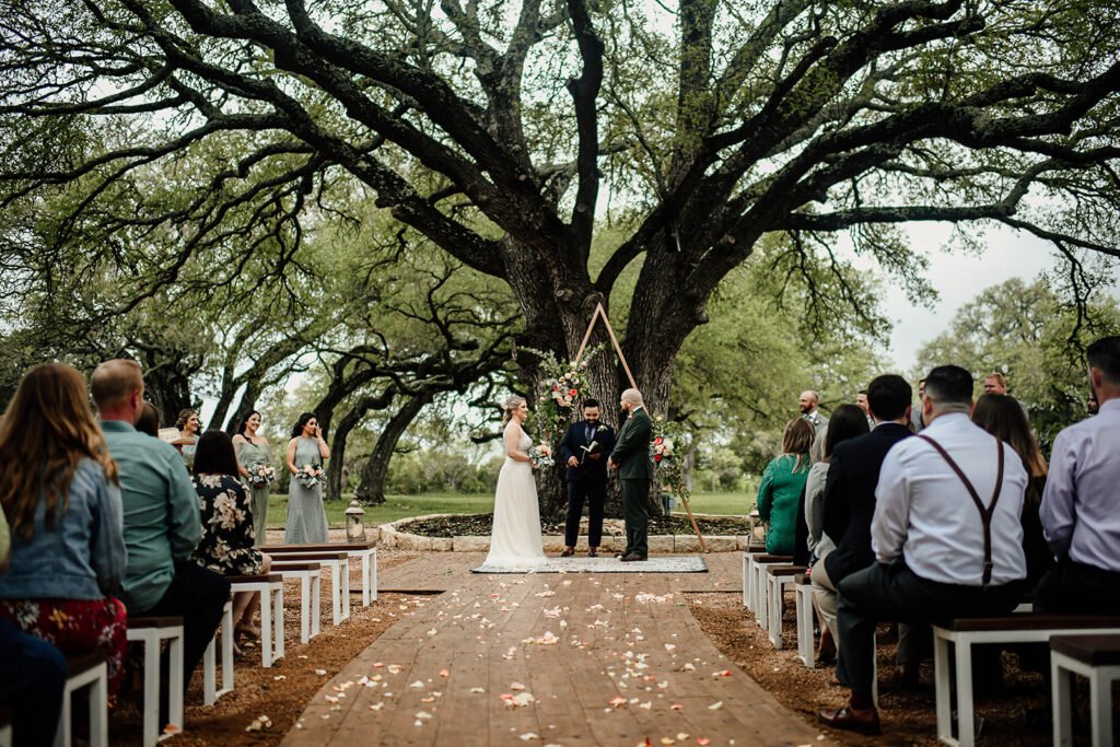 Everything You Need to Know About Texas Pre-Nuptial Agreements. Austin Texas Wedding Venue outdoor ceremony featuring historic oak trees, luxury seating, bride and groom exchanging vows as wealthy wedding guests enjoy the wedding. 