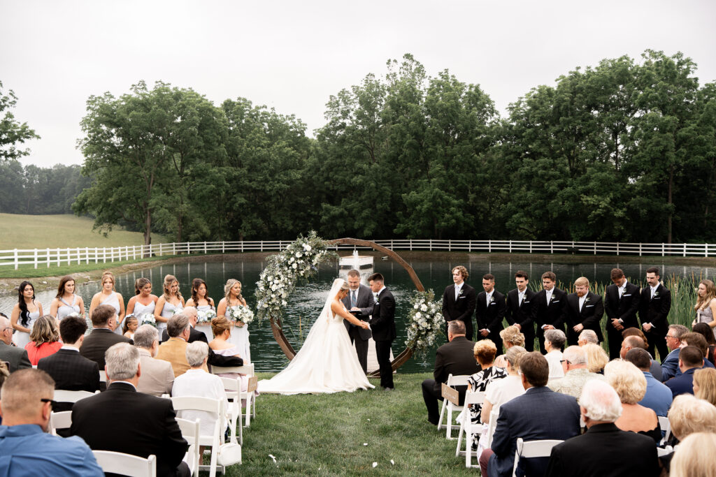 Bride & groom exchange vows at a garden wedding ceremony featuring a pond & fountain with wedding guests who travelled from Philadelphia, New Jersey, Maryland and beyond.