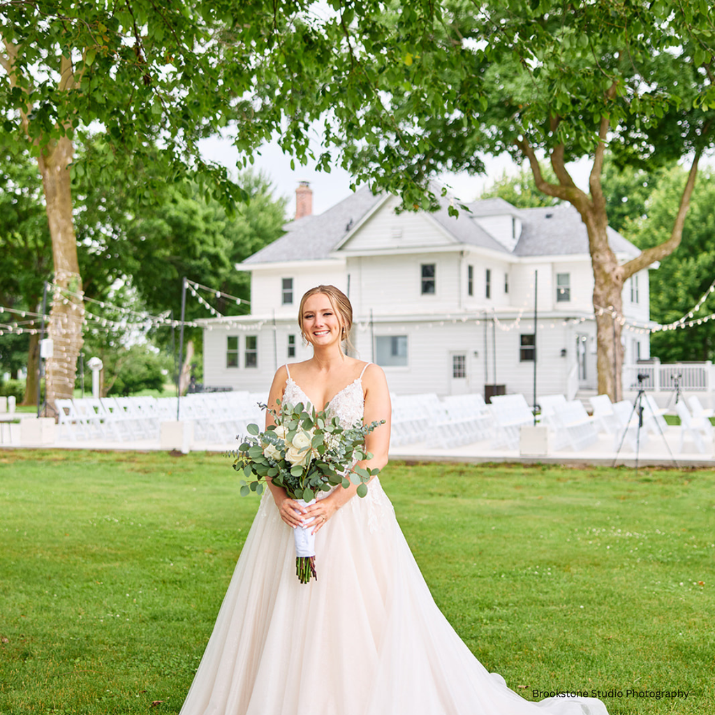 Bride holding luxury flowers poses in front of the garden outdoor wedding ceremony at Pole Barn Chic, an independently owned Springfield wedding venue